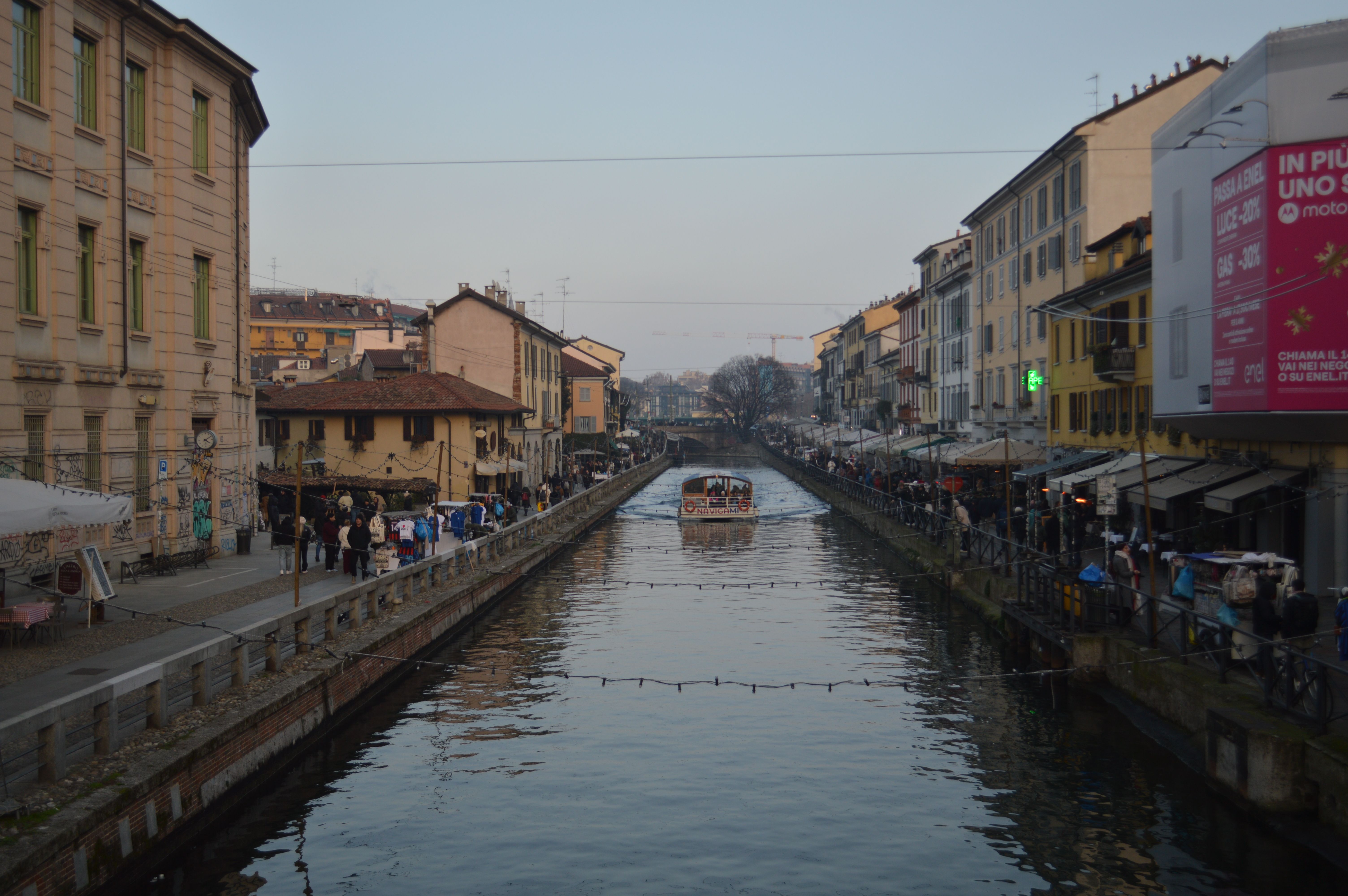 A canal in the Navigli district of Milan at dusk, with bars and people along both banks.