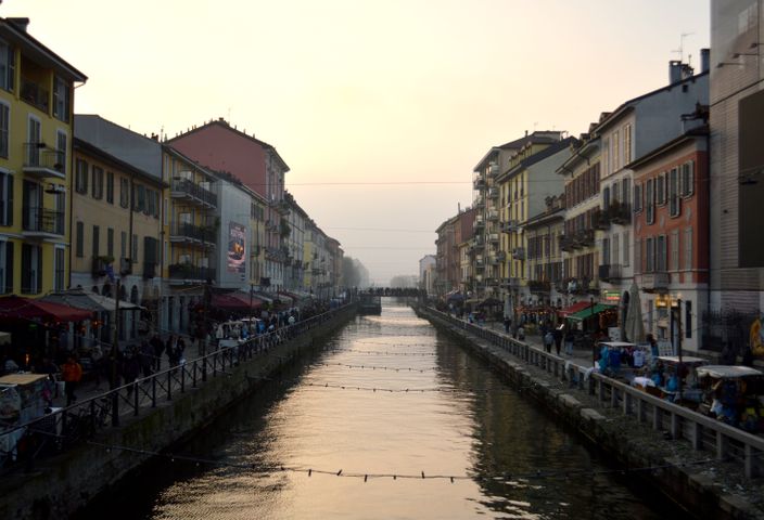 View of Naviglio Grande canal at sunset in Milan, Italy, flanked by colorful buildings and bustling streets.