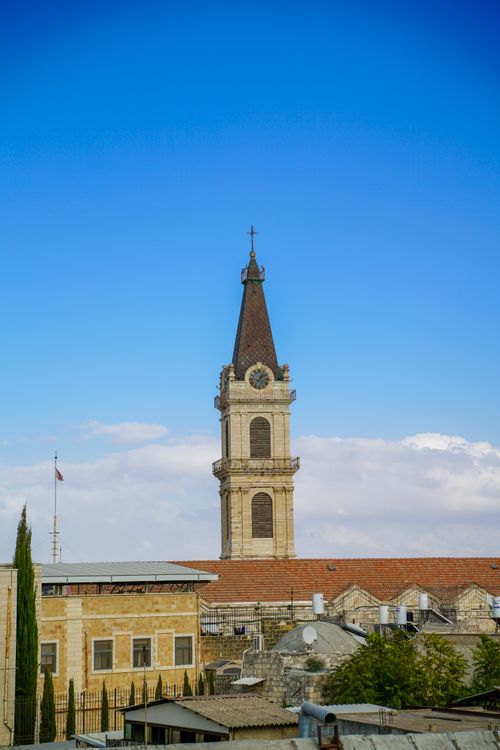 Free A historic clock tower rises above urban rooftops beneath a clear blue sky, embodying architectural beauty. Stock Photo