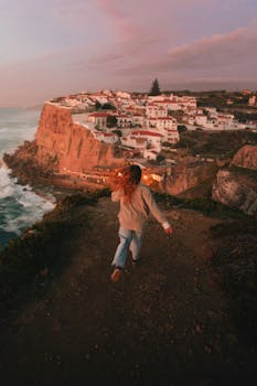 Woman running at sunset towards Azenhas do Mar village in Portugal with stunning coastal cliffs.