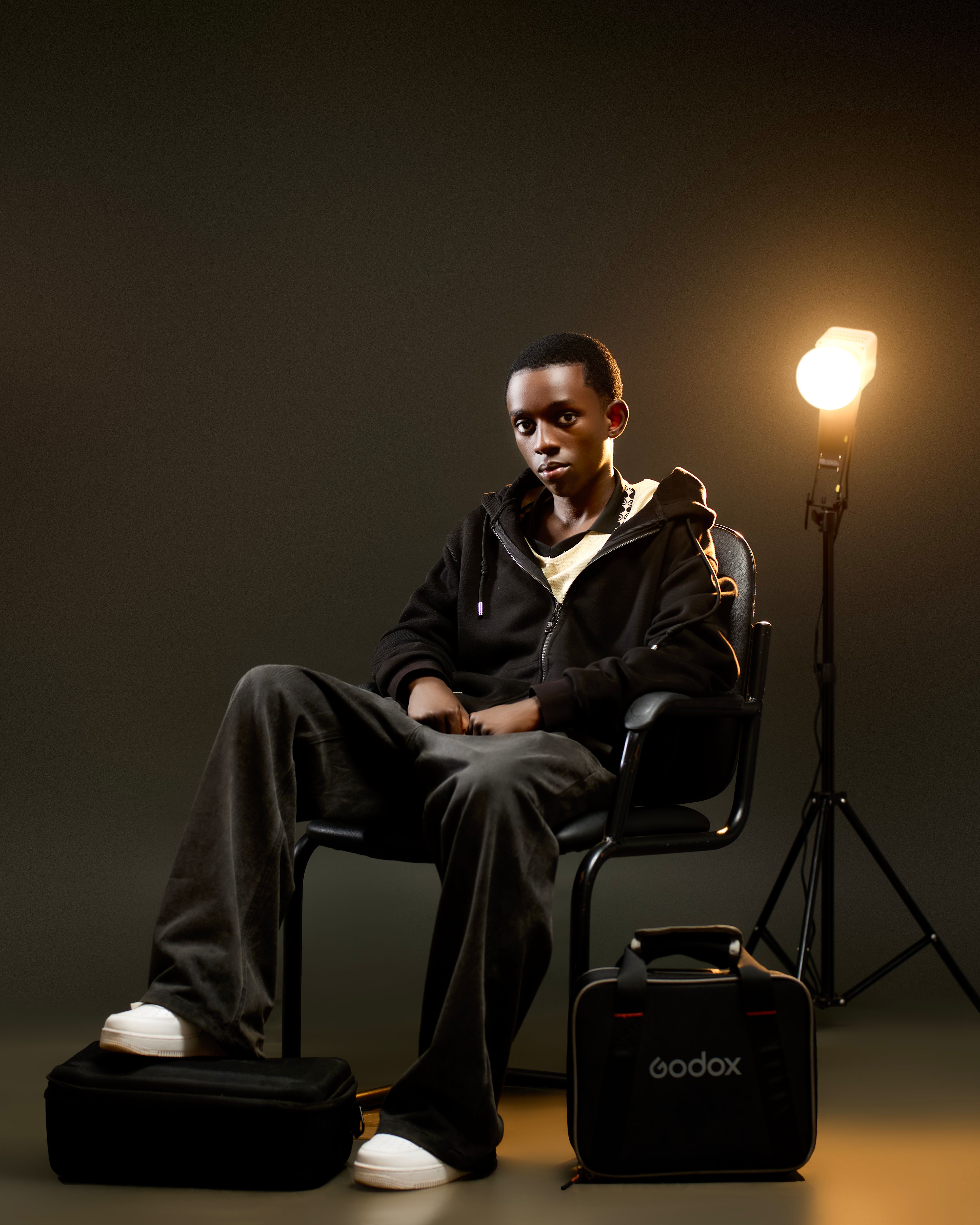 A young man seated calmly in a studio with professional lighting equipment.