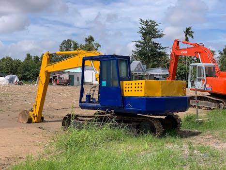 Vibrant blue and orange excavators parked at an outdoor construction site under a sunny sky.