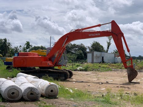 Orange excavator at a construction site on a sunny day with cloudy sky.
