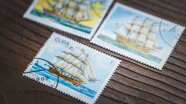 Close-up of vintage Cuban postage stamps displaying sailing ships on a wooden background.