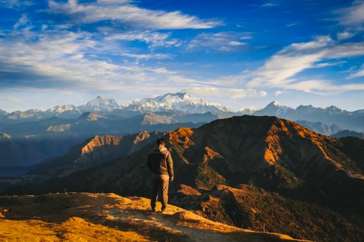 A person stands on a mountain peak, overlooking a stunning sunrise over the Himalayas.