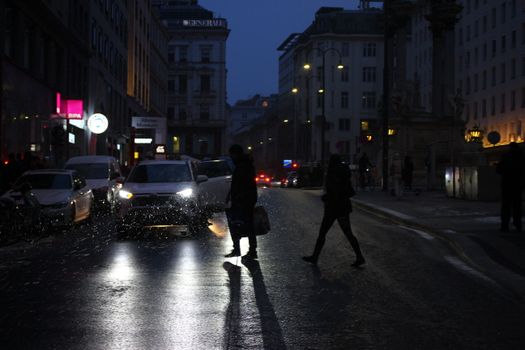 Silhouettes crossing a dimly-lit street in Vienna, Austria at dusk.