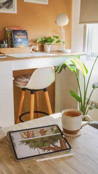 A cozy indoor workspace with an iPad displaying an illustration, a coffee cup, and plants.