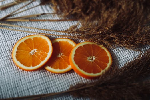 Vibrant orange slices on a textured white surface with dried grass for an autumn feel.