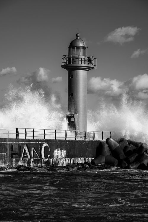 Free A striking black and white image of a lighthouse with waves crashing dramatically against it. Stock Photo