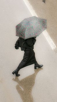 Aerial view of a stylish woman walking on a rainy street holding a colorful umbrella.