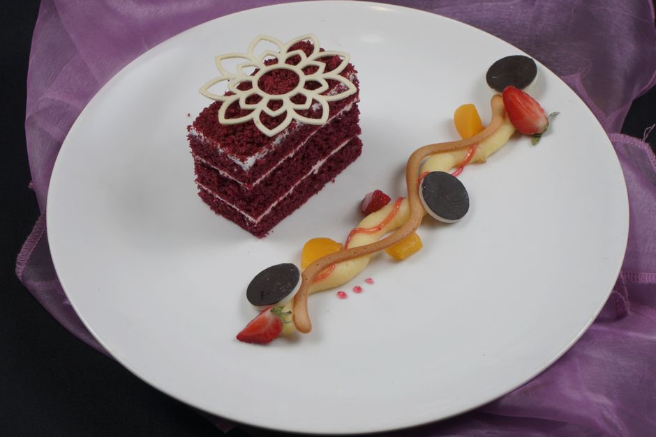 A two-layer red velvet cake with white cream cheese frosting, sliced to reveal a deep red crumb, sitting on a white cake stand.