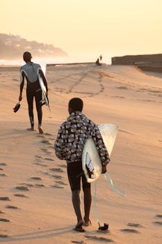 Two surfers carrying boards on Durban beach during a golden sunrise.