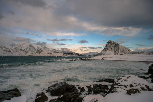 Free Stunning view of the Lofoten Islands fjord with snow-covered mountains, rocky shore, and cloudy sky. Stock Photo