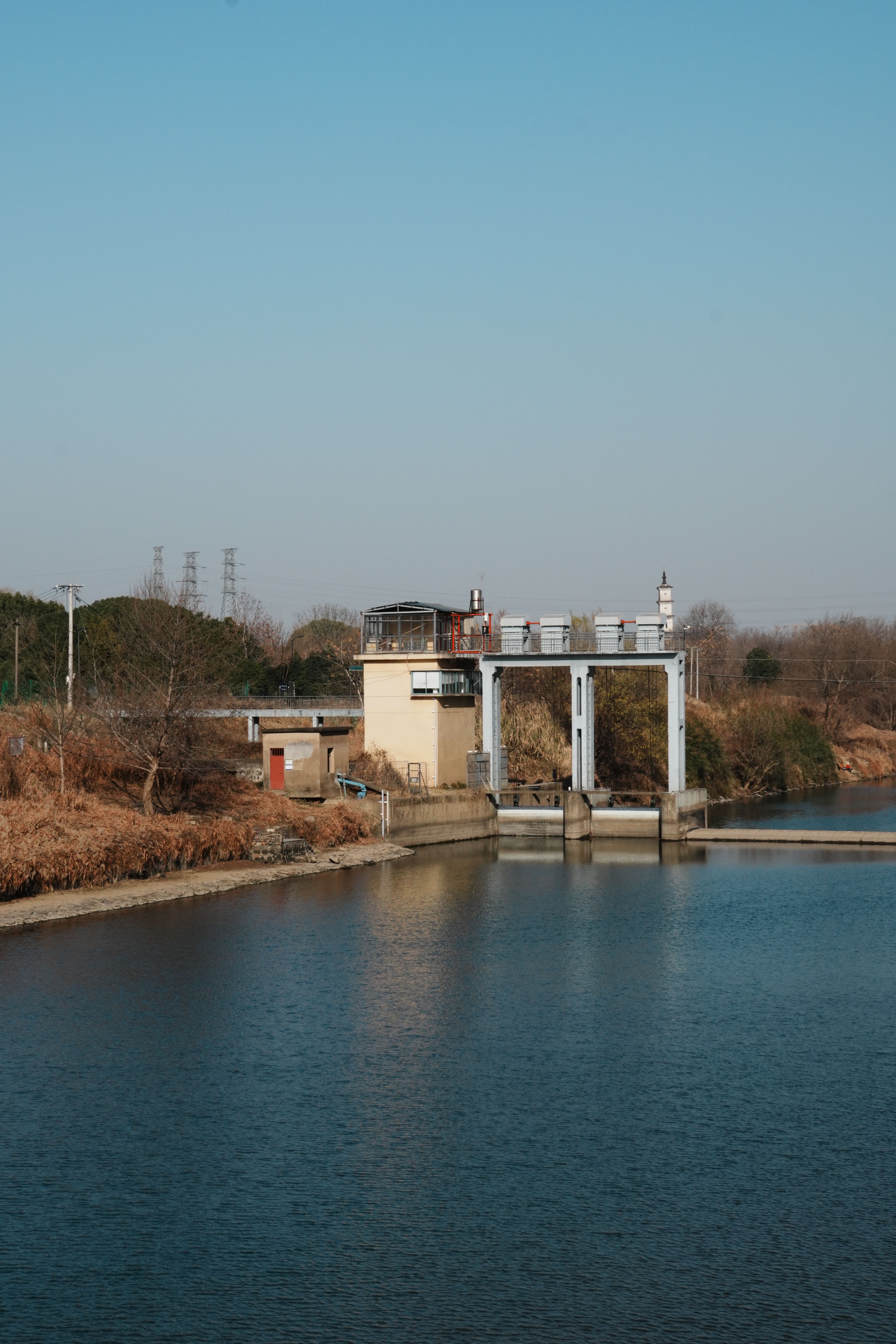 Pumping station by the river with a clear sky, surrounded by dry foliage during winter.