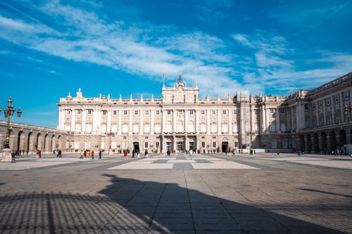 Free View of the Royal Palace of Madrid with blue sky and scattered visitors. Stock Photo