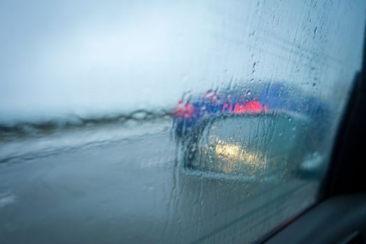 Close-up of rain-covered car window with blurred road and vehicle lights, creating a moody, wet atmosphere.