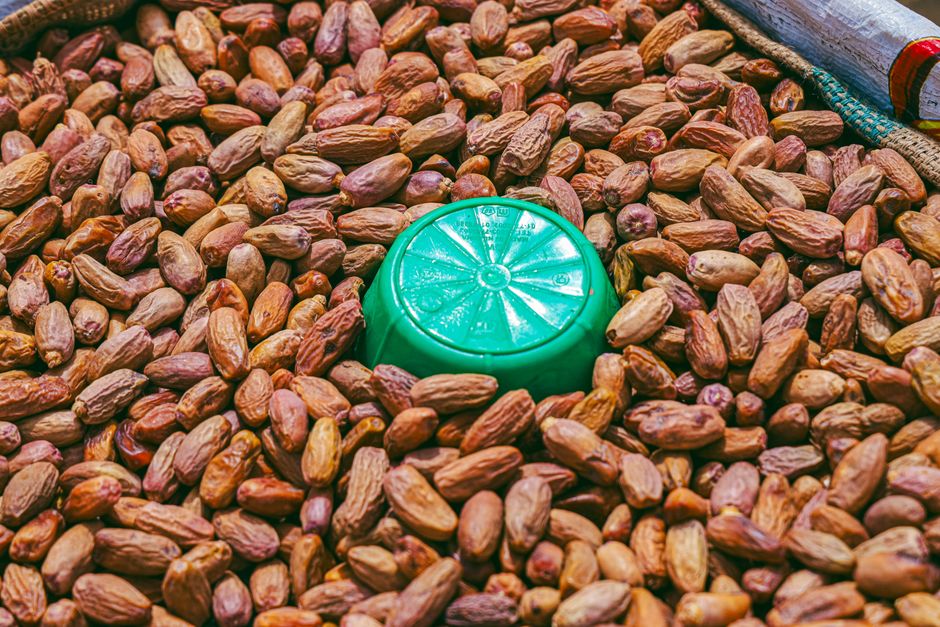 Close-up image of dry date palm fruits with a green plastic bowl in a market setting.