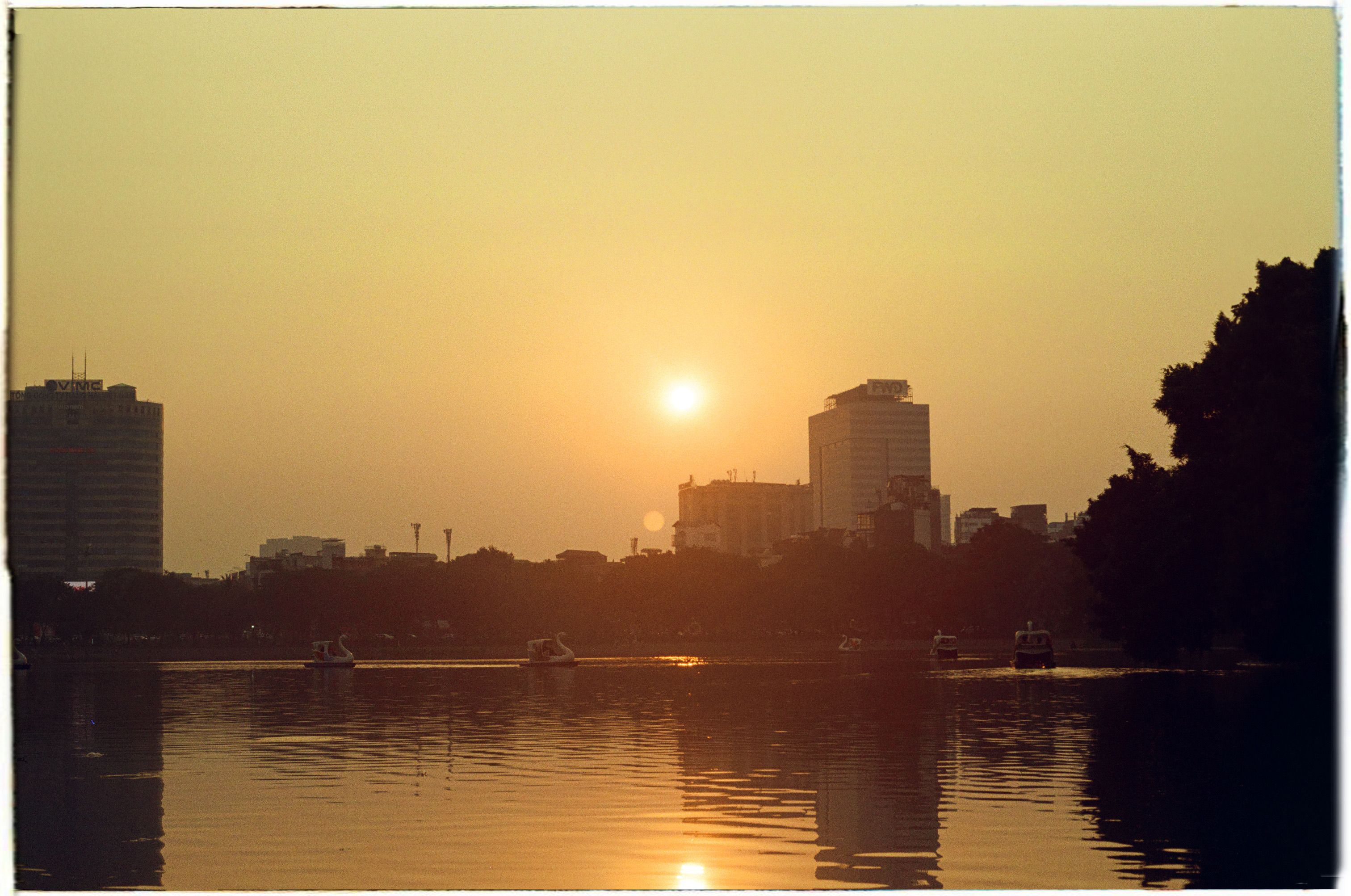 Beautiful sunset over a city skyline with a calm lake and boats reflecting the urban tranquility.