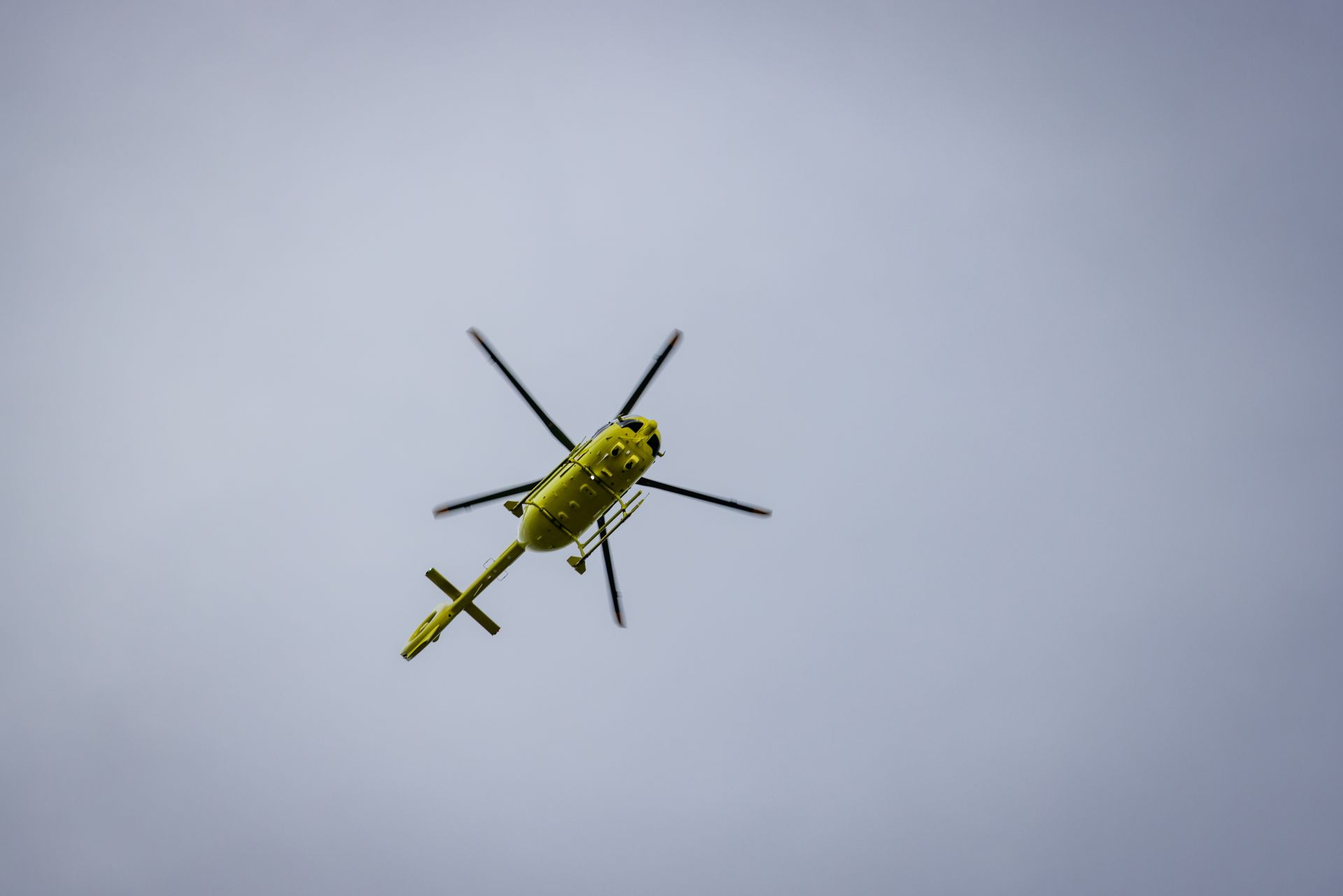 A vibrant yellow helicopter seen flying against a clear blue sky.
