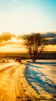 A car on a snowy road during a vibrant winter sunset with scenic rural landscape.
