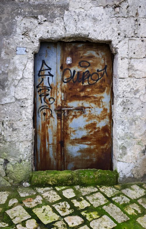 Free A rustic metal door with graffiti on a stone building, featuring a textured surface. Stock Photo