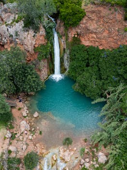 Aerial view of a stunning waterfall cascading into a turquoise pool surrounded by lush greenery in Faro, Portugal.