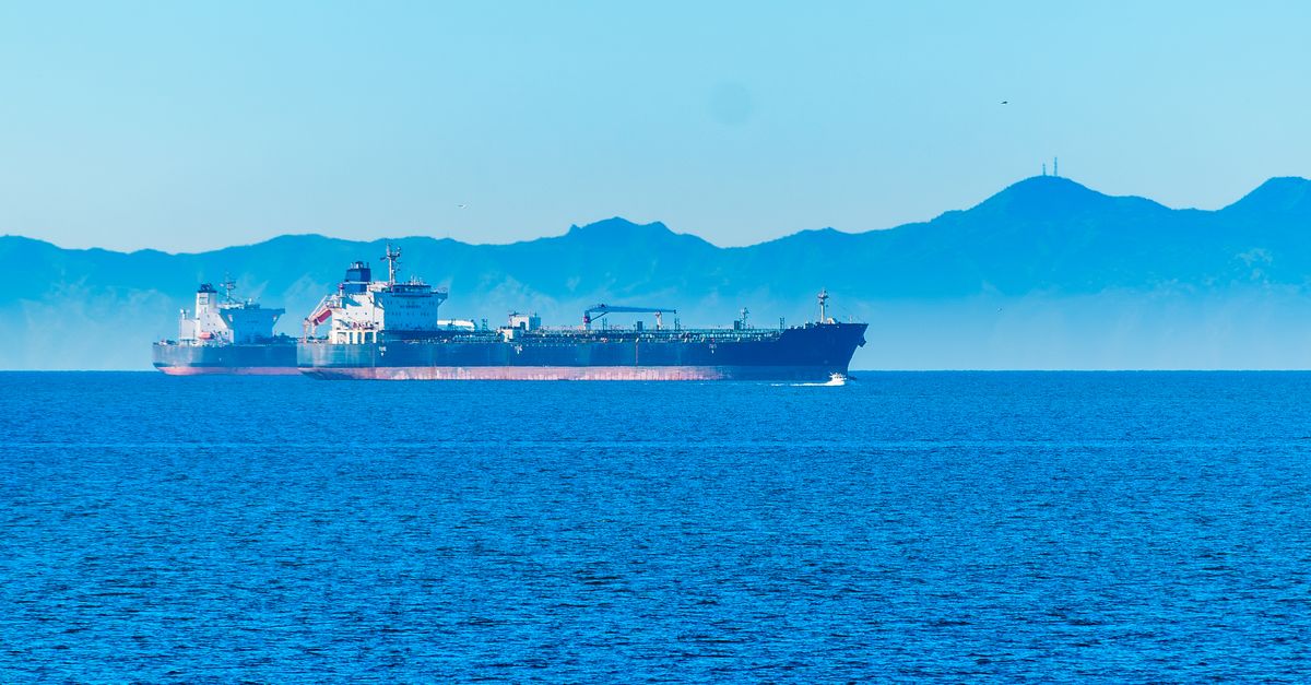 An orange offshore drilling platform stands in calm blue waters under a bright, clear sky.