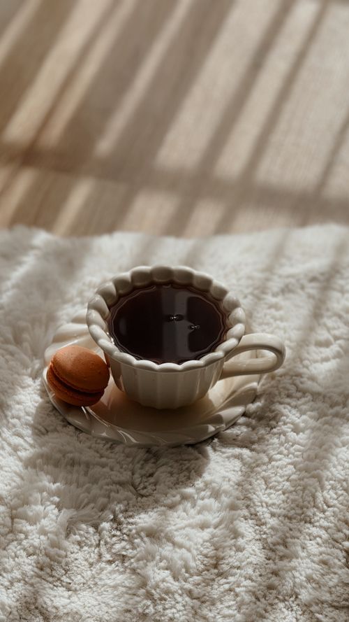 Free A cup of coffee with a macaron on a cozy rug lit by sunlight. Stock Photo