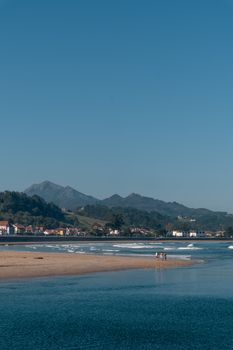 Scenic view of a peaceful beach with distant mountains and small village in Asturias, Spain.