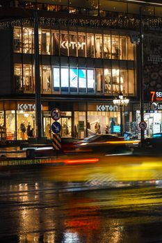 City street at night showcasing illuminated shopfront and blurred traffic lights.