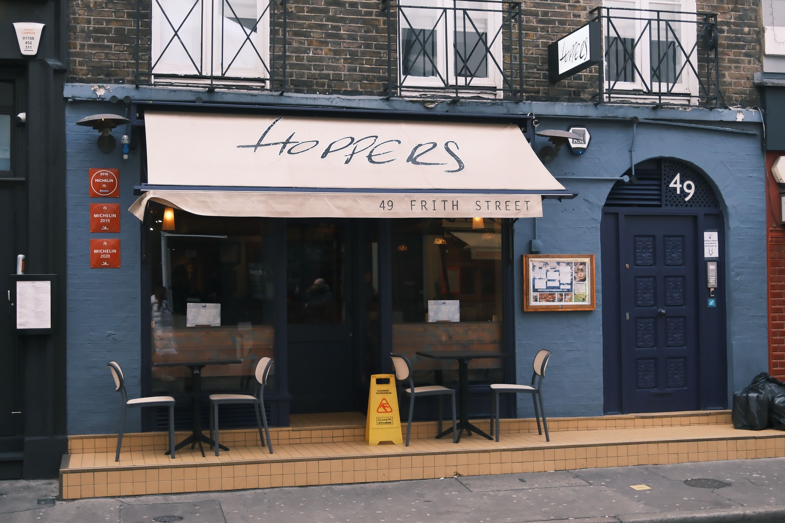Front view of Hoppers, a cozy restaurant on Frith Street, London, featuring outdoor seating and Michelin signs.