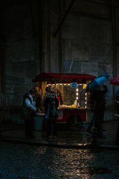 Rainy night scene at a street market in Istanbul with people and umbrellas.