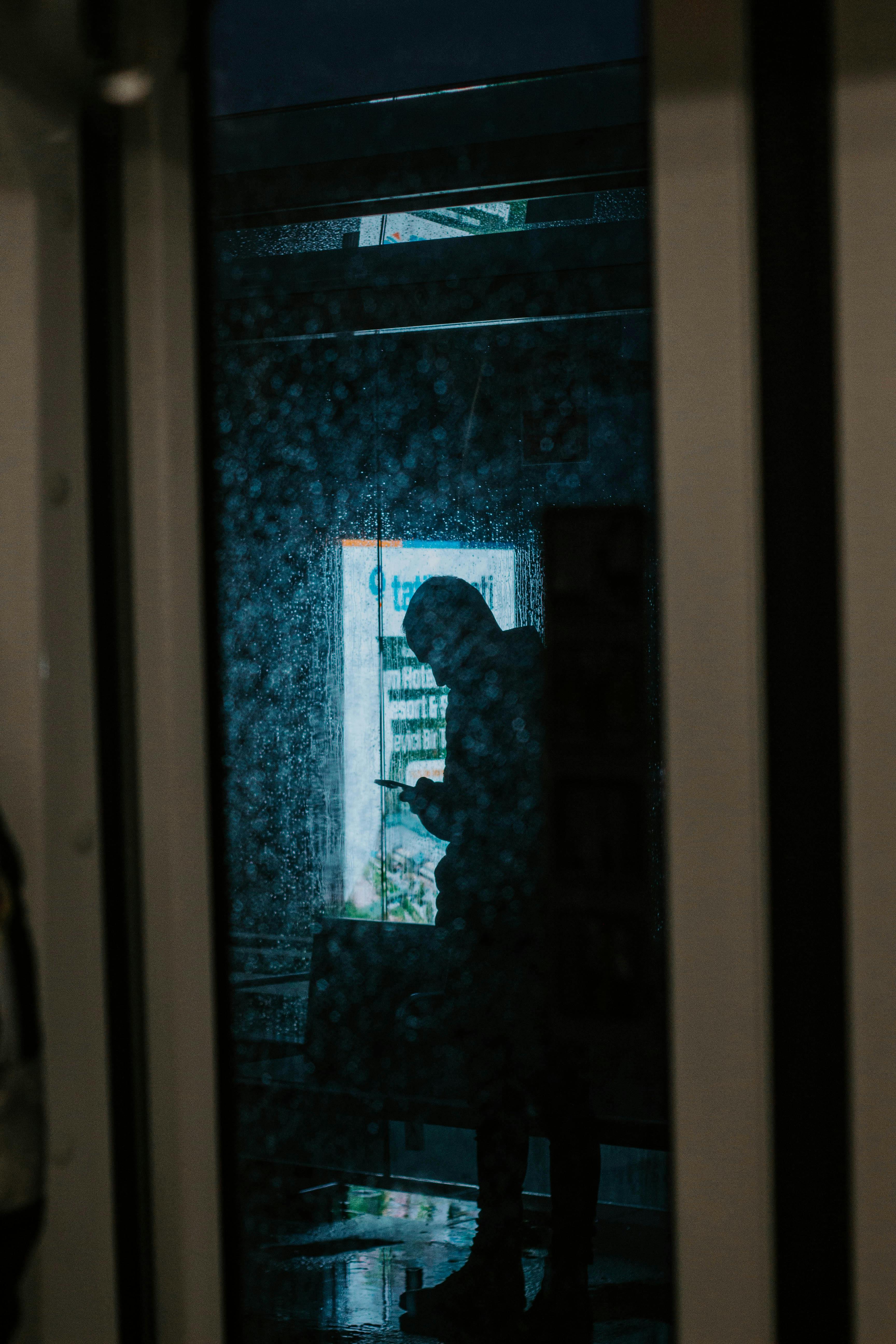 grátis Silhueta de uma pessoa usando o celular, refletida na janela em um dia chuvoso em Istambul. Foto profissional