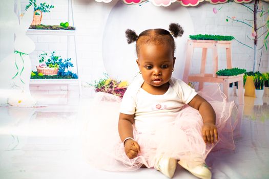 Cute baby girl in a pink tutu sitting indoors with floral background.