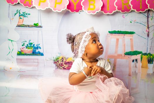 Cute toddler in a pink tutu enjoying a vibrant birthday celebration indoors.