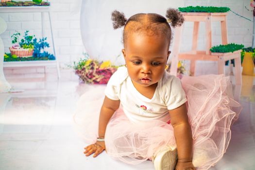 Charming baby girl plays in a pink tulle skirt on a bright indoor set.