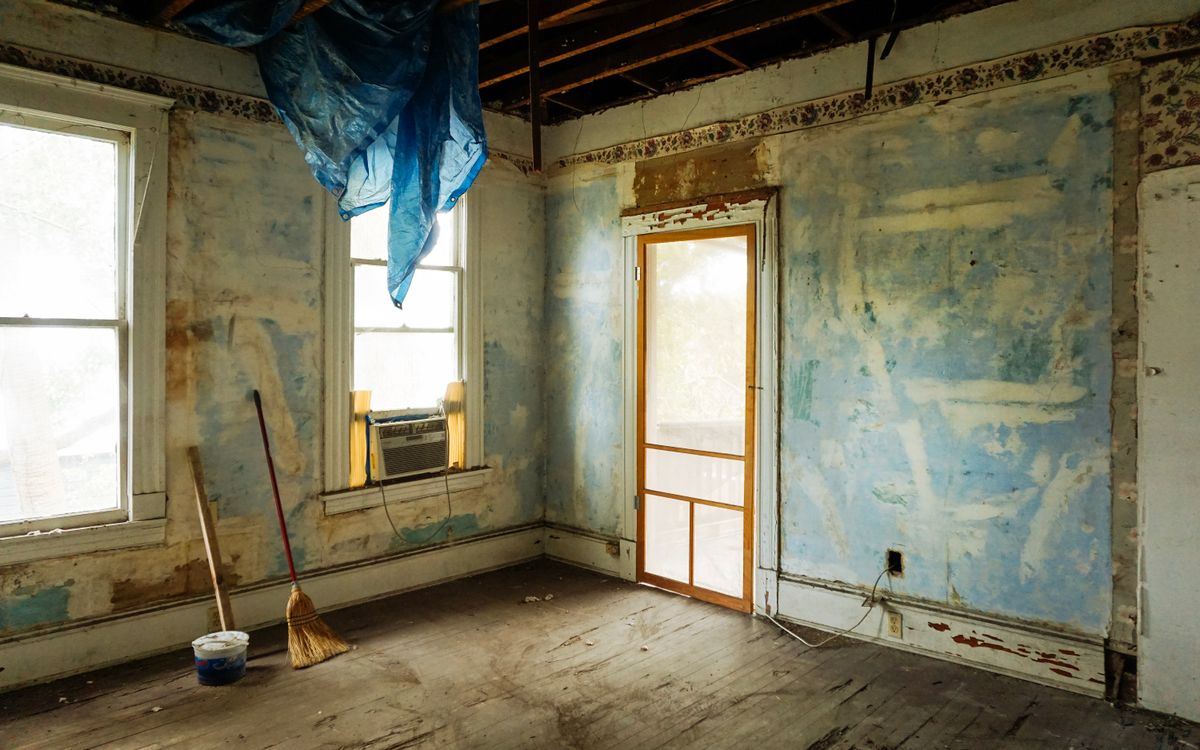 An empty room in an abandoned house with peeling walls and construction tools.
