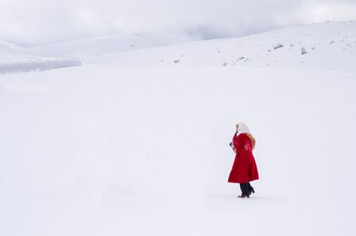 Free A person in a red coat walks through a vast snowy landscape, evoking solitude and winter chill. Stock Photo