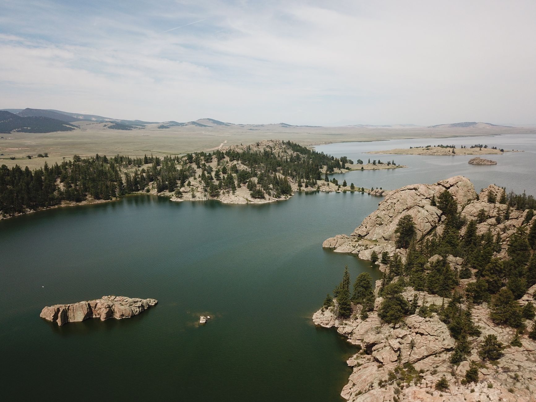 Aerial view of a picturesque lake surrounded by rocky formations and dense forest in Colorado, USA.