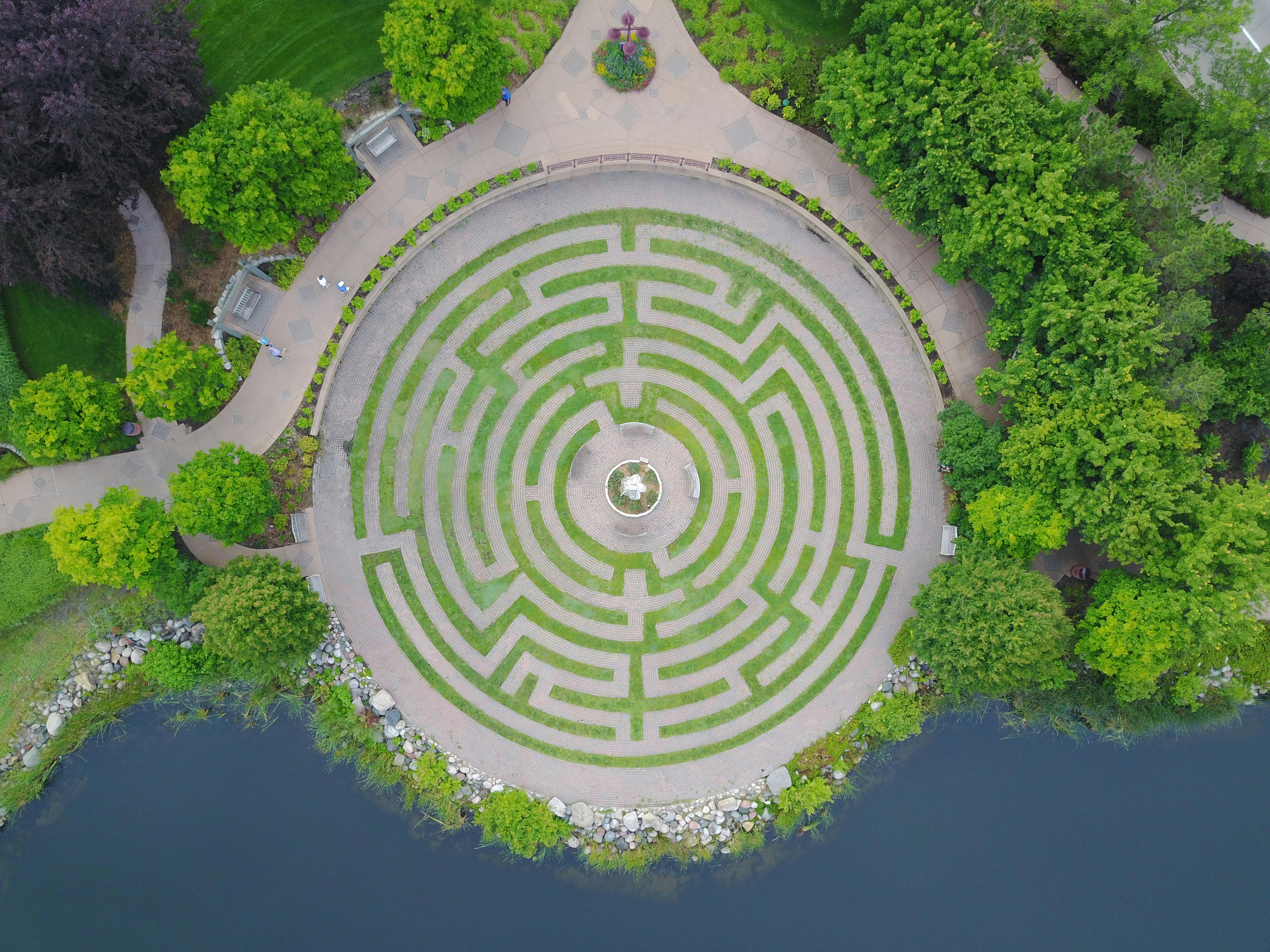 Discover an aerial perspective of a circular garden maze surrounded by greenery and water.