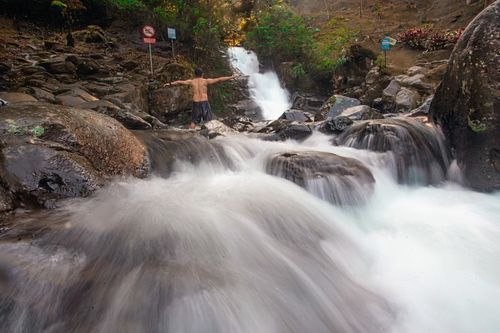 Free A man stands by a waterfall amidst lush greenery, embracing nature's beauty. Stock Photo