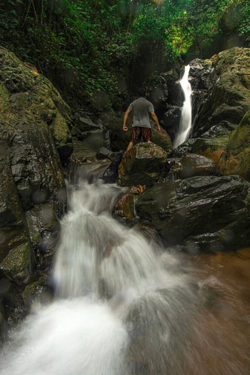 Free A person navigates rocks while exploring a vibrant jungle waterfall. Stock Photo
