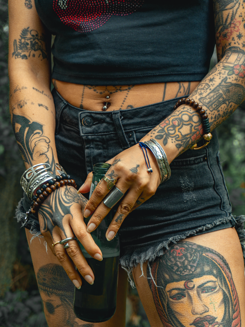Free Close-up of a tattooed woman wearing various bracelets and rings, holding a drink outdoors. Stock Photo
