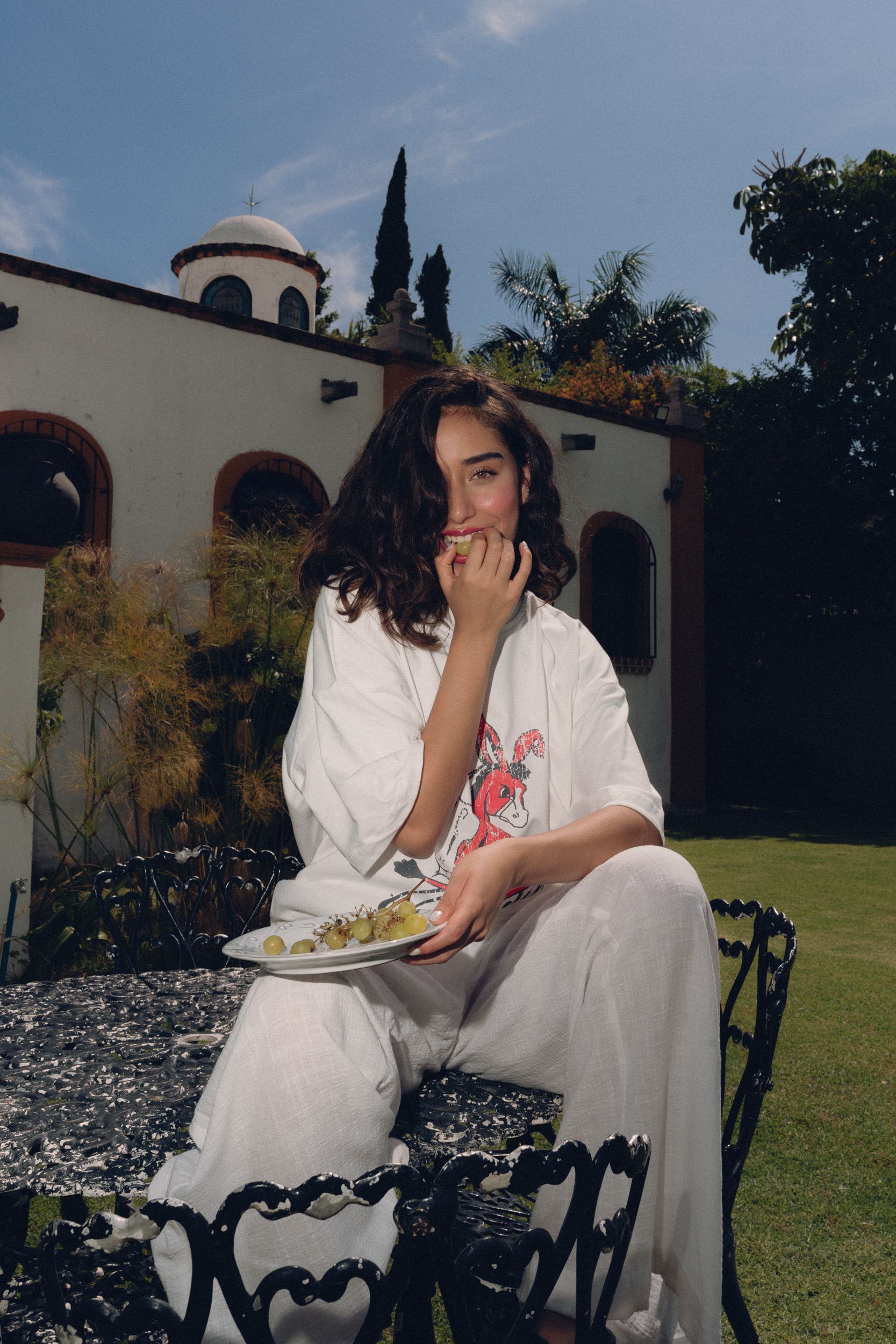Young woman seated outdoors, savoring a plate of food in a garden setting.
