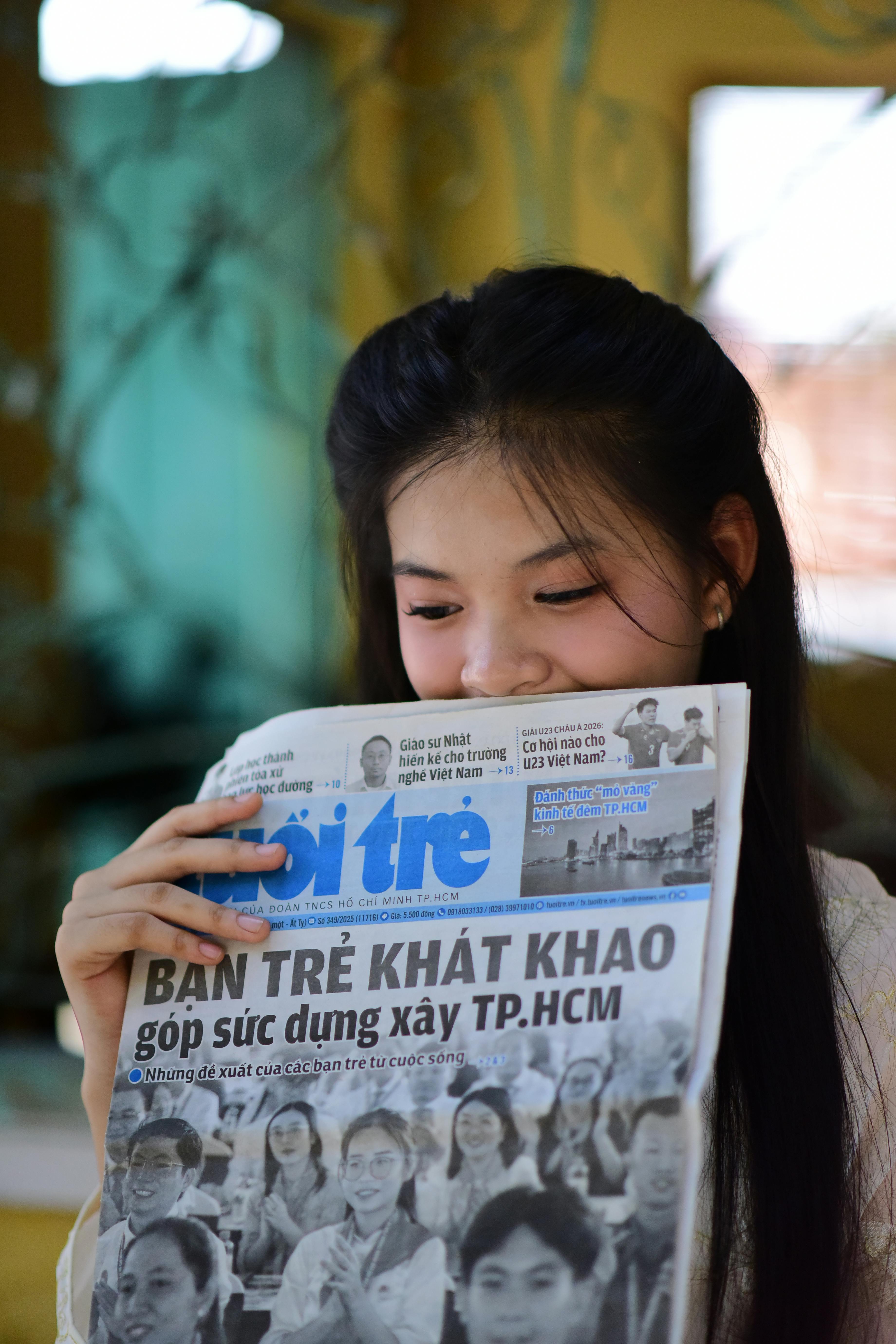 Young woman smiling and reading a Vietnamese newspaper indoors. Bright and engaging moment captured.