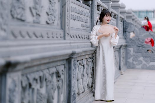 Woman in traditional attire holding a fan by an ornate wall.