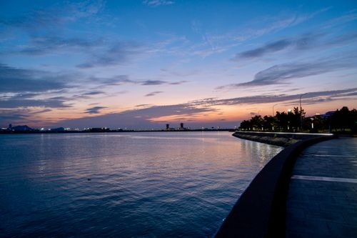 Free Tranquil coastal scene at sunset with calm waters and distant city lights. Stock Photo