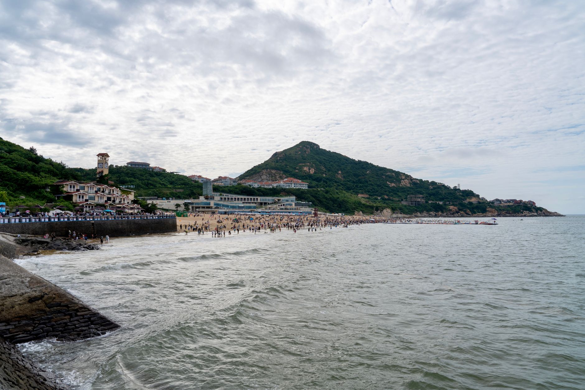 A bustling beach scene with scenic mountain backdrop and cloudy sky.