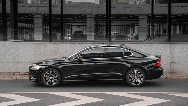 Side view of a modern black sedan parked against a city wall.