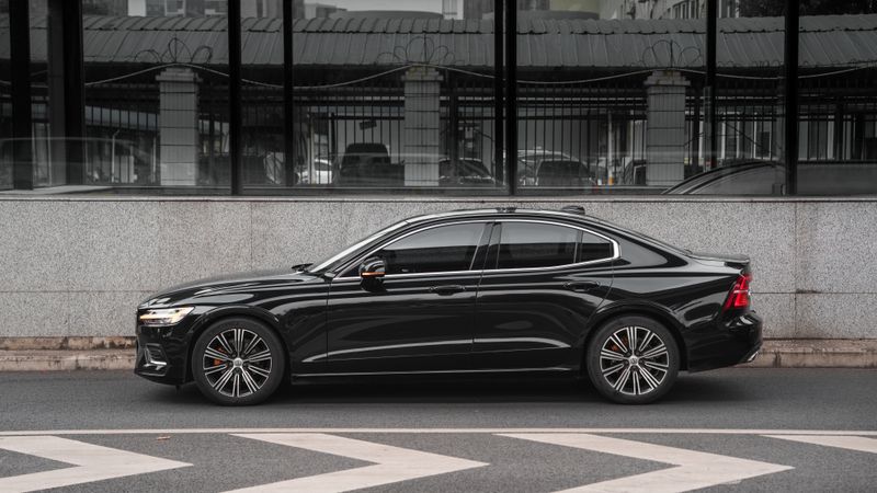 A black sedan waiting at the kerb beside a city wall, photo by Oli Liao on Pexels